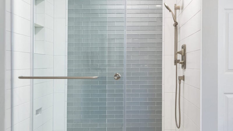 Walk-in shower with gray glass tile accent wall